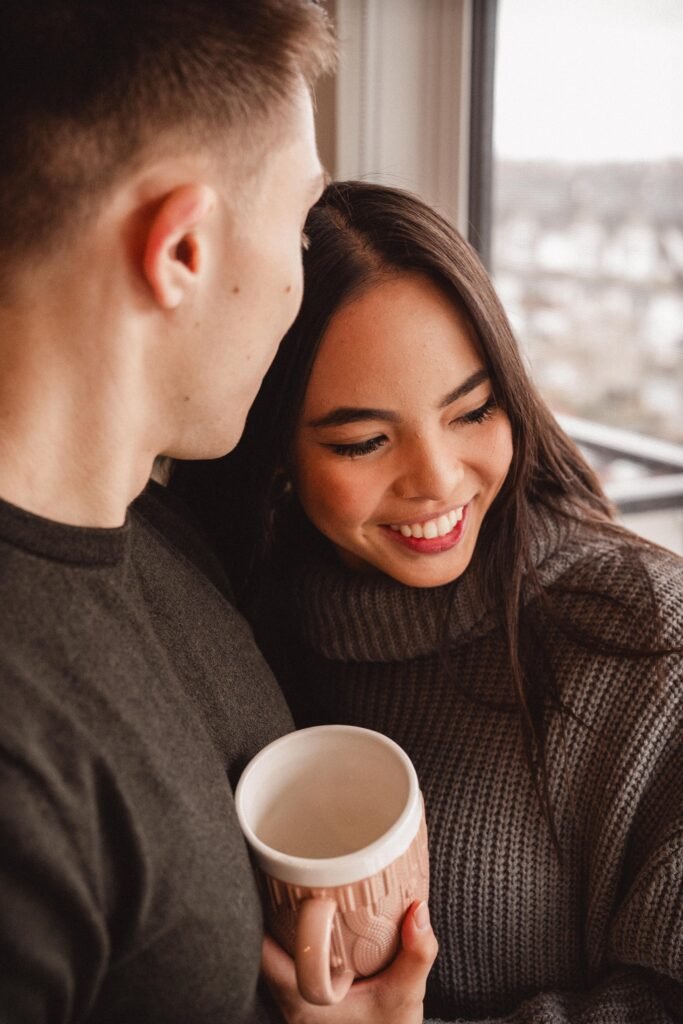 Warmth and joy fill the air as a couple dances near a Christmas tree with mugs of hot chocolate in hand, a moment captured during a holiday photoshoot with Zur Photography.